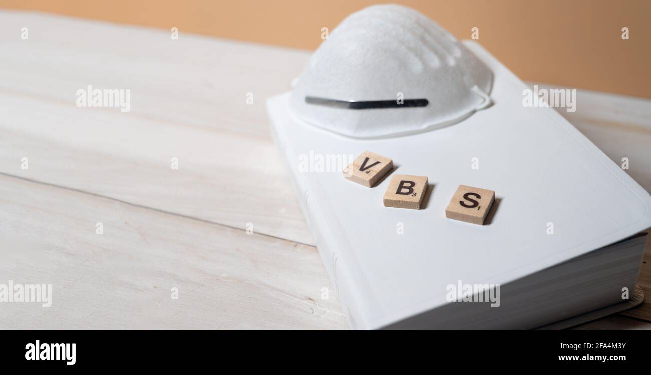 VBS for Vacation Bible School Spelled in wooden Letters with face mask over white bible. Re-opening of Church. selected focus. Christian concept. copy Stock Photo