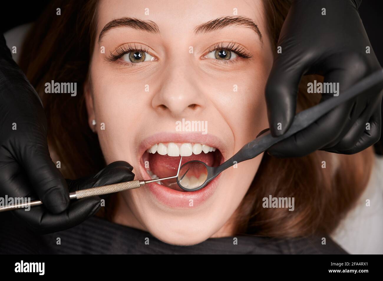 Close up of dentist hands in black sterile gloves examining female