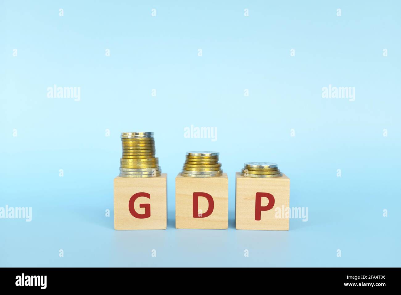 GDP or gross domestic product letters in wooden blocks with decreasing stack of coins. Economic crisis, decline and recession concept. Stock Photo