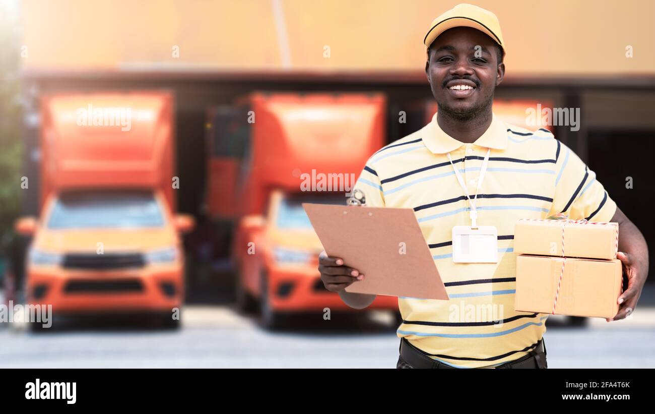 African male postal delivery courier man holding delivering package boxs in front of car Stock Photo