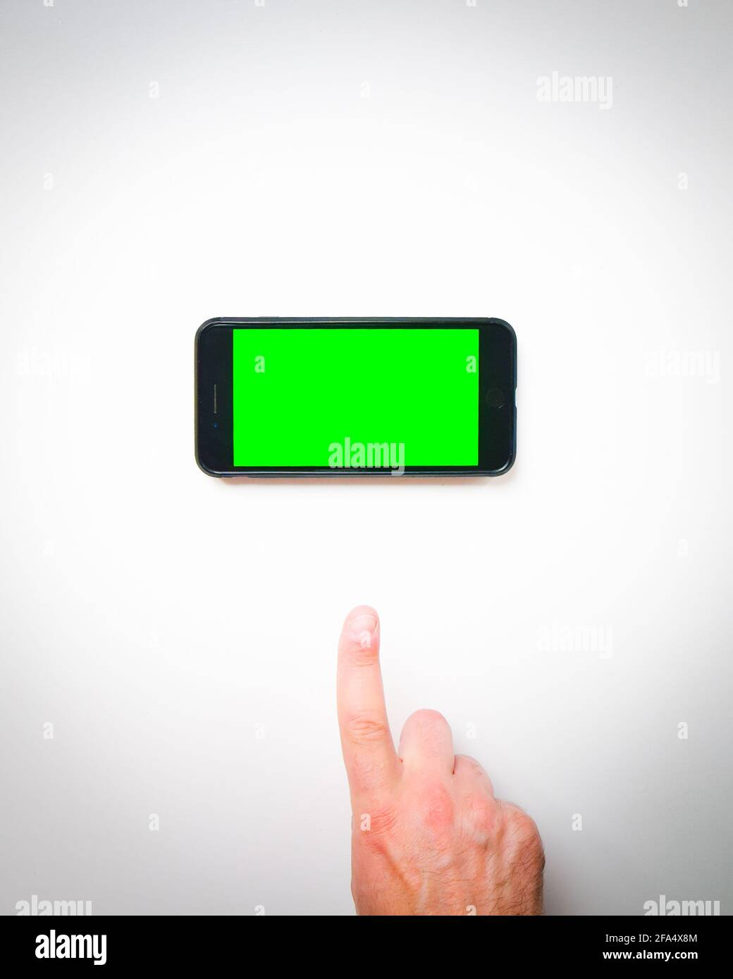 Male hand finger up to smartphone green screen on a white background curtains. Isolated blank space copypaste smartphone background mock up Stock Photo