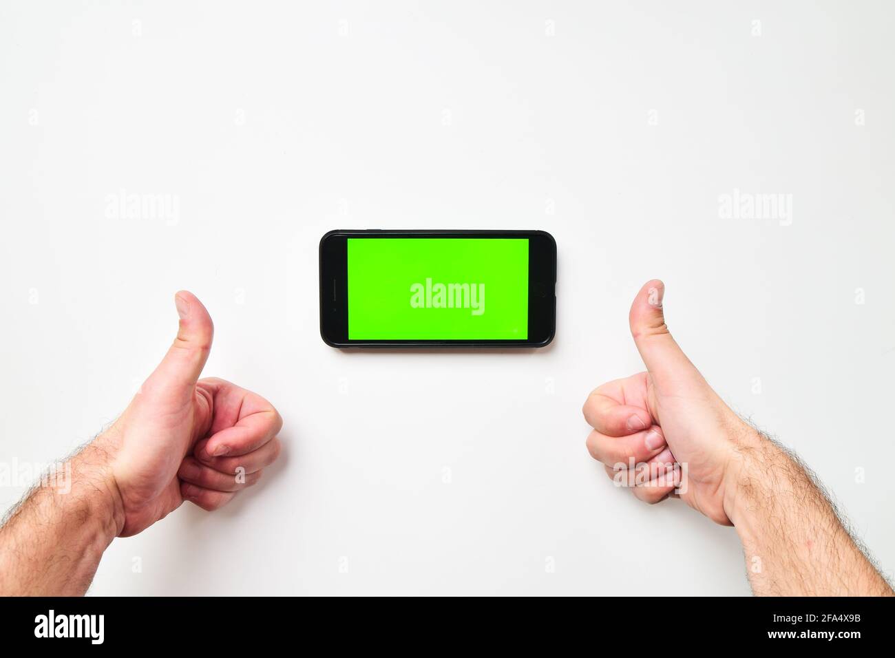 Male big hands and mobile smartphone with green screen in horizontal position background with two hand thumbs up finger. Mock up mobile screen blank s Stock Photo