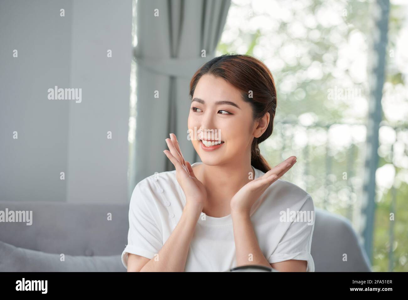 Beautiful young woman is touching her face and smiling while looking at ...