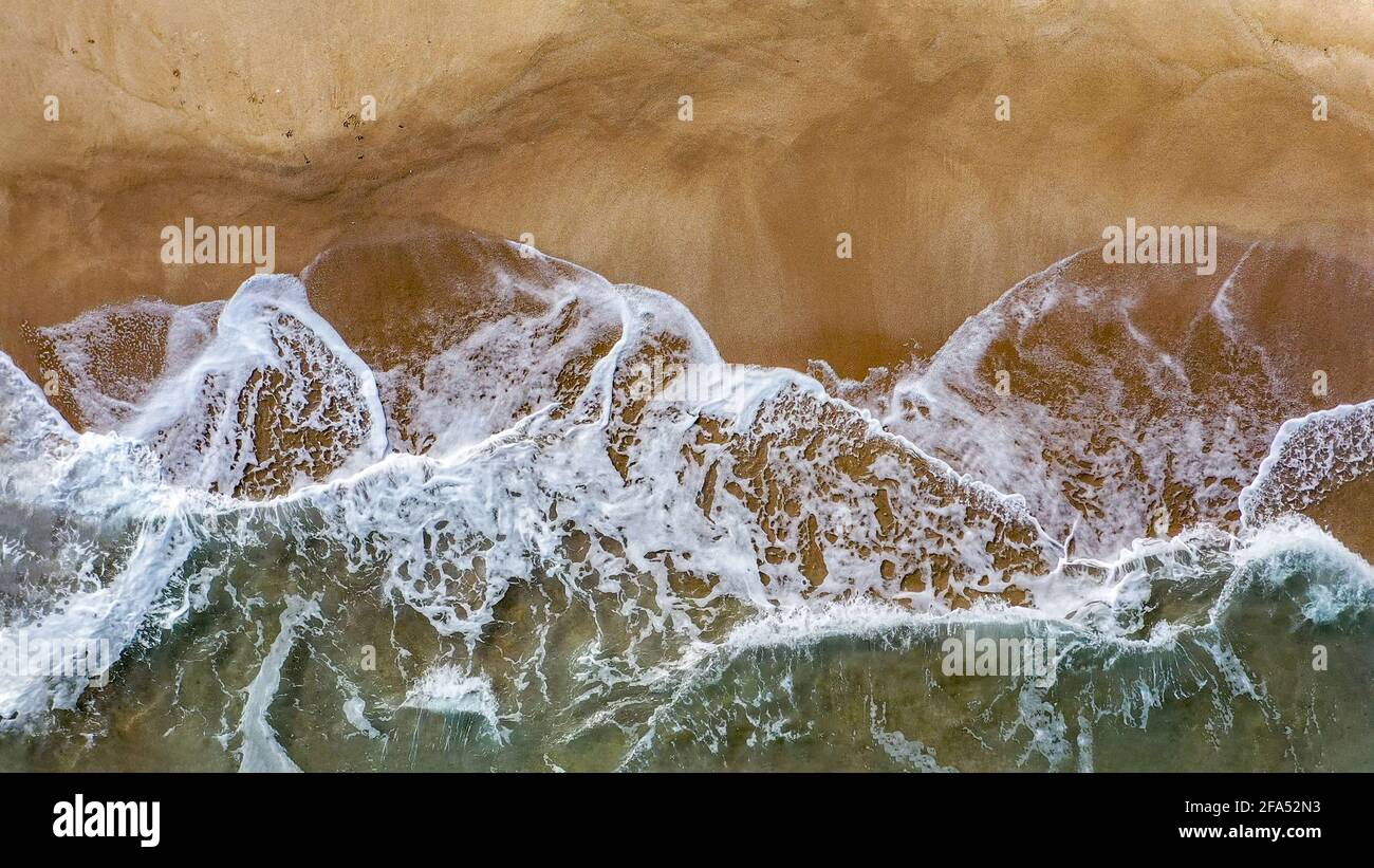 Aerial image of sea waves crashing on a beach in a summer afternoon Stock Photo