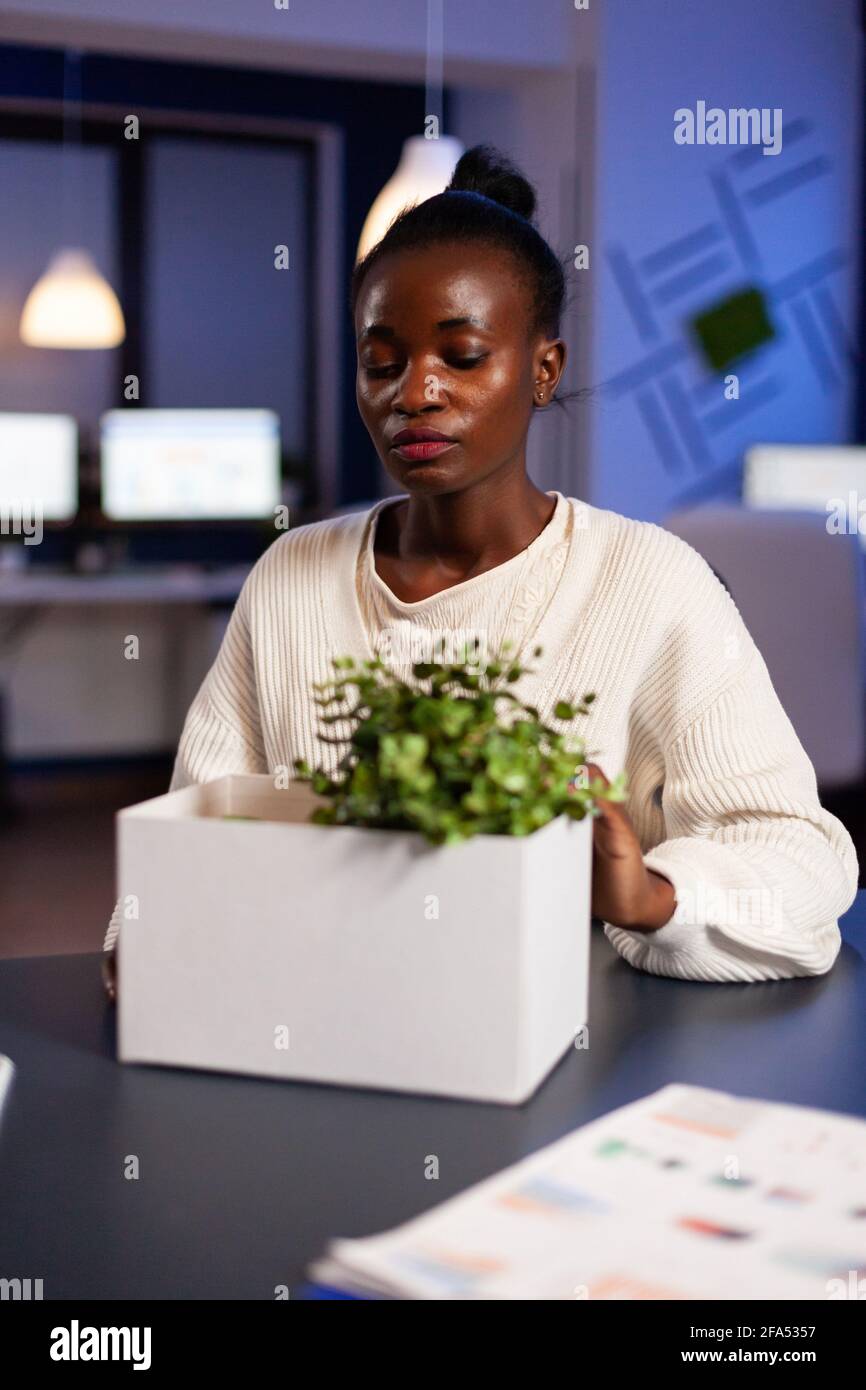 African managar sad after being dismissed from work taking belongings. Unemployed packing things late at night. woman leaving workplace office in midnight. Stock Photo