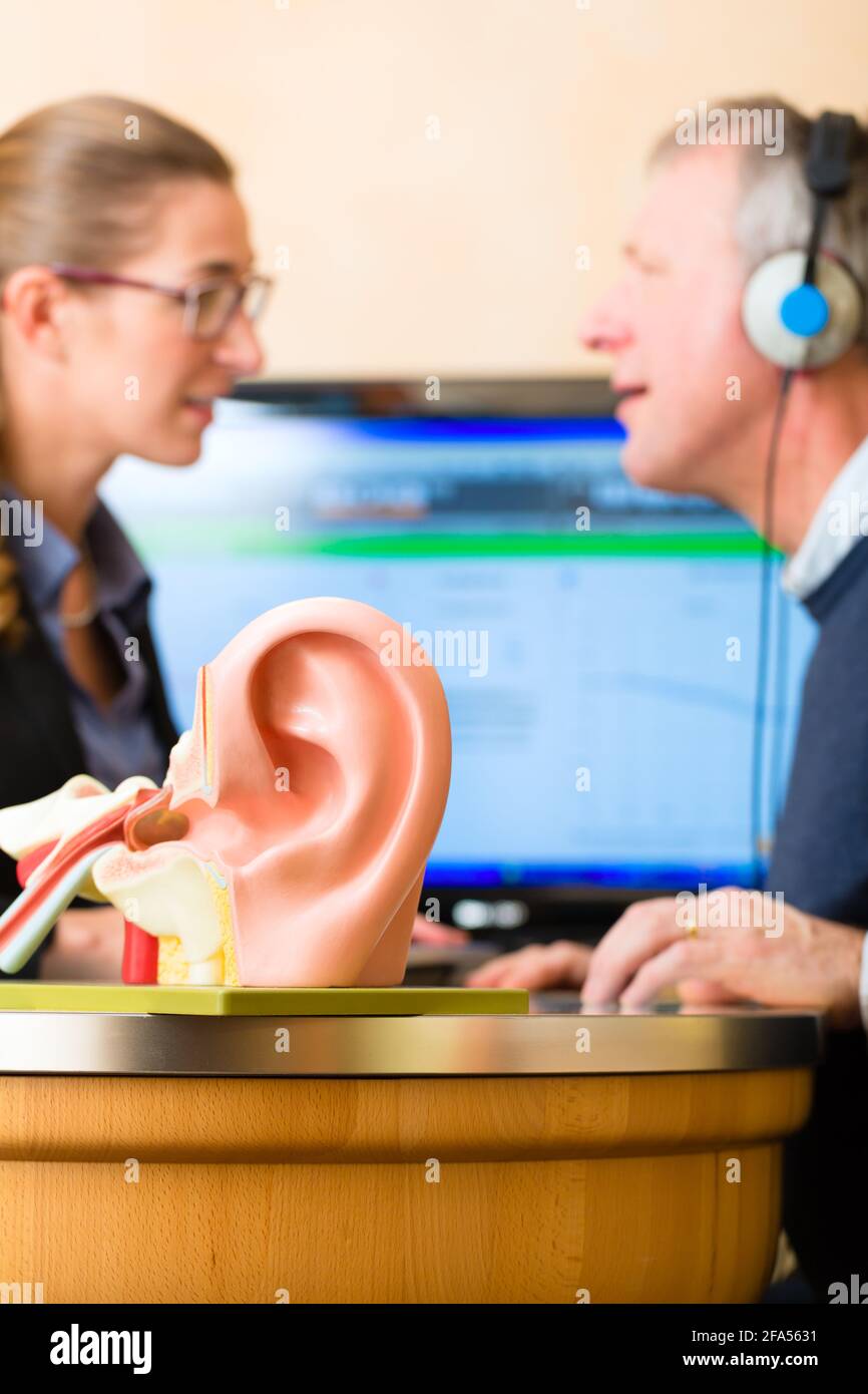 Older man or pensioner with a hearing problem make a hearing test and may need a hearing aid, in the foreground is a model of a human ear Stock Photo