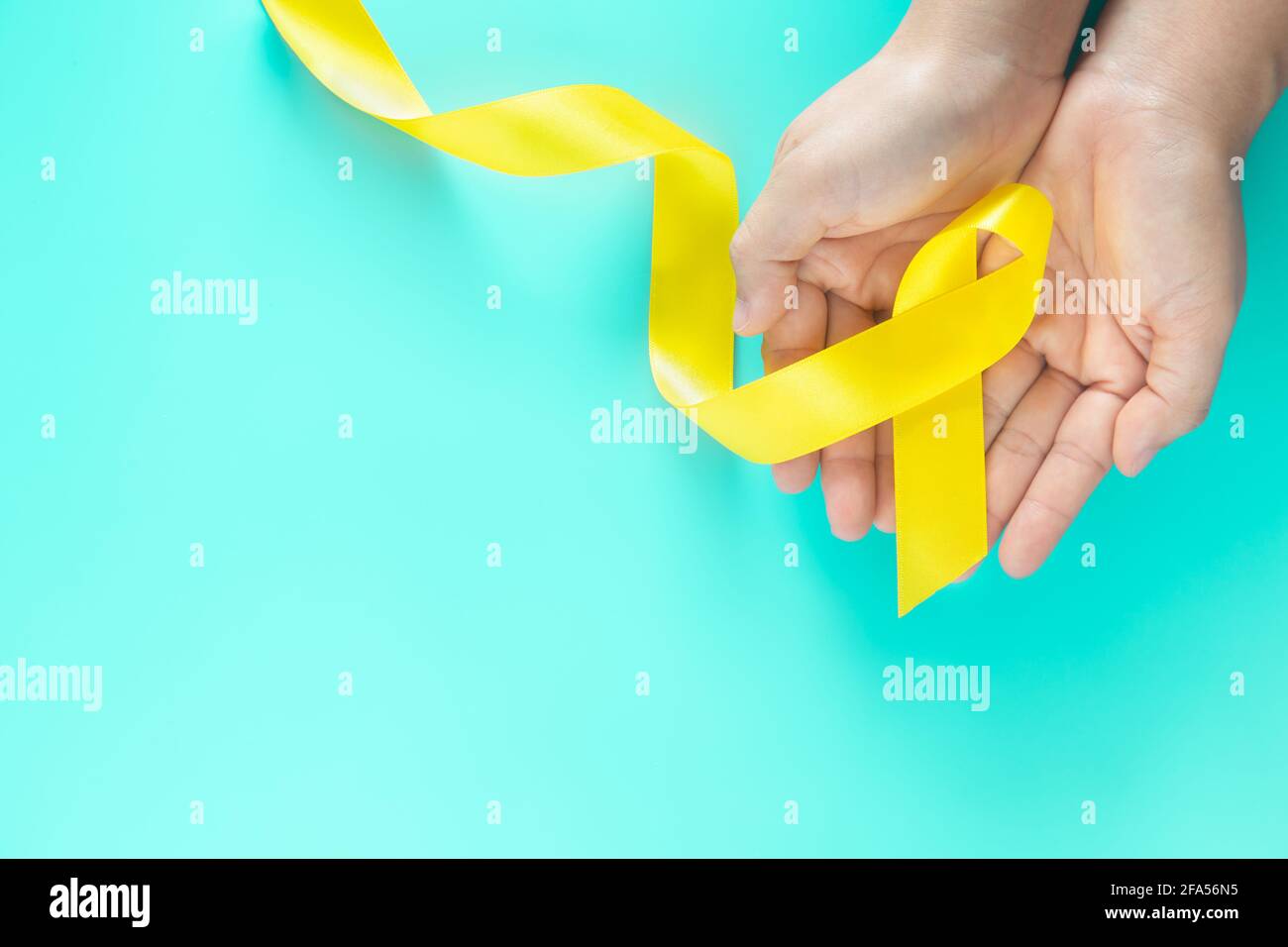 Hand holding Yellow ribbon on green background, copy space. Bone cancer Sarcoma Awareness childhood cancer cholangiocarcinoma gallbladder cancer world Stock Photo