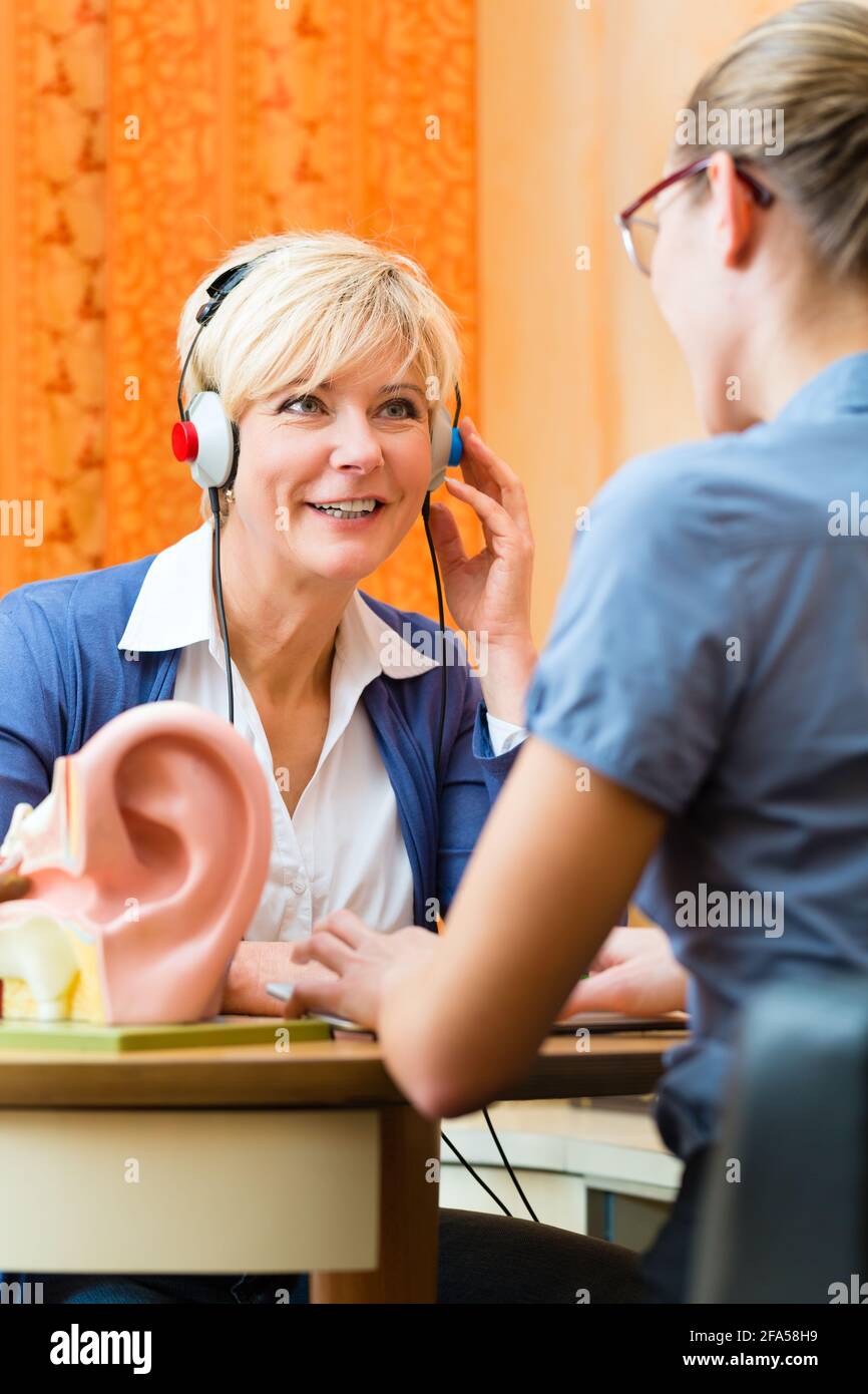 Older woman or female pensioner with a hearing problem make a hearing test and may need a hearing aid, in the foreground is a model of a human ear Stock Photo