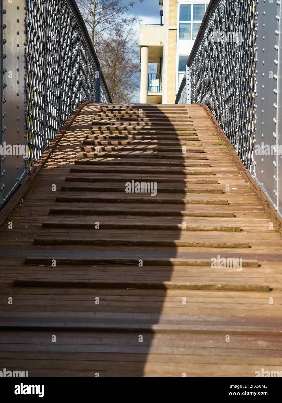 A small wooden footbridge over the water at Greenland Docks, seen from a low angle and with an emphasis on the rhythm of shadow and material. Stock Photo