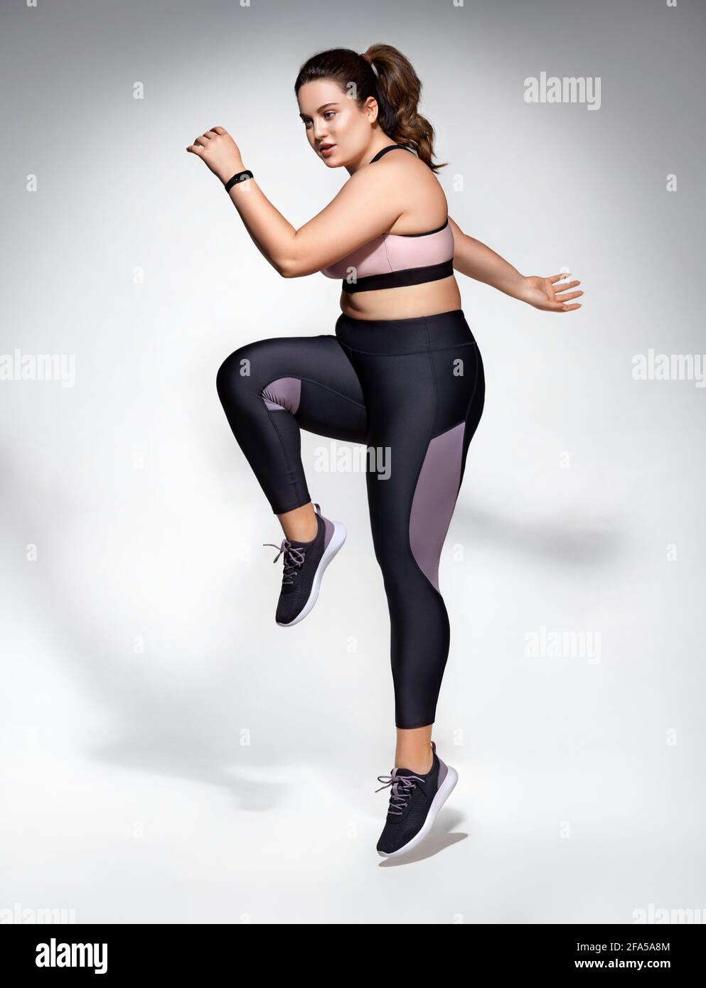 Sporty woman jumping. Photo of model with curvy figure in fashionable  sportswear on grey background. Sports motivation and healthy lifestyle  Stock Photo - Alamy