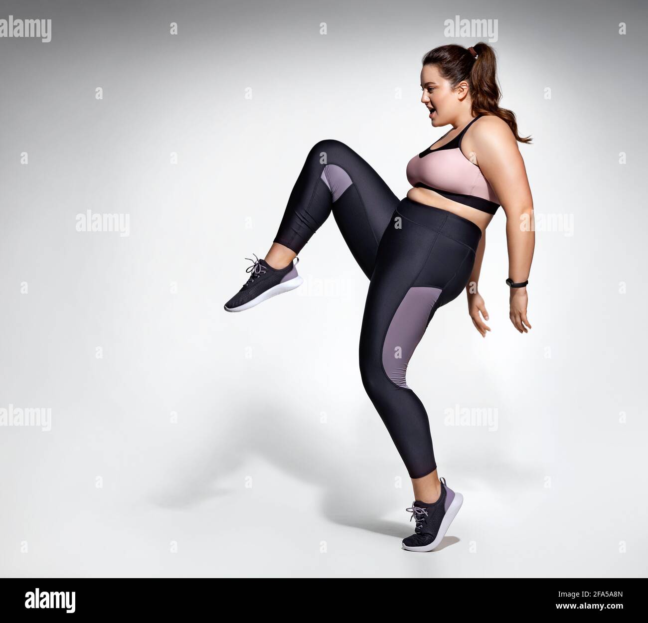 Girl practicing exercise, performs kick up. Photo of model with curvy  figure in fashionable sportswear on grey background. Sports motivation and  healt Stock Photo - Alamy