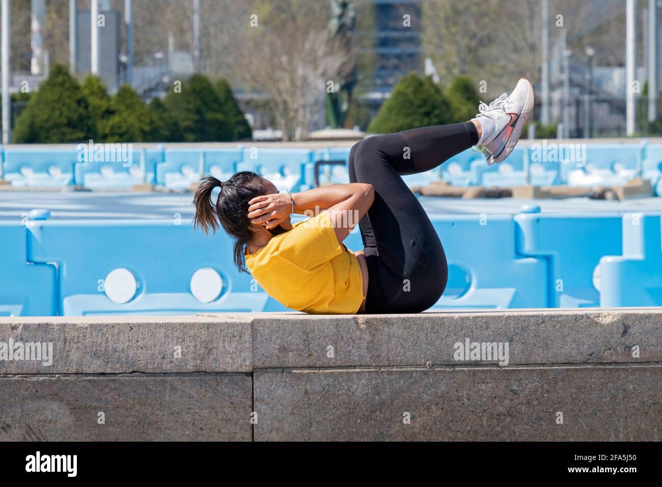 A very fit woman does crunch exercises on a ledge near the Unisphere in Flushing Meadons Corona Park in Queens, New York City. Stock Photo