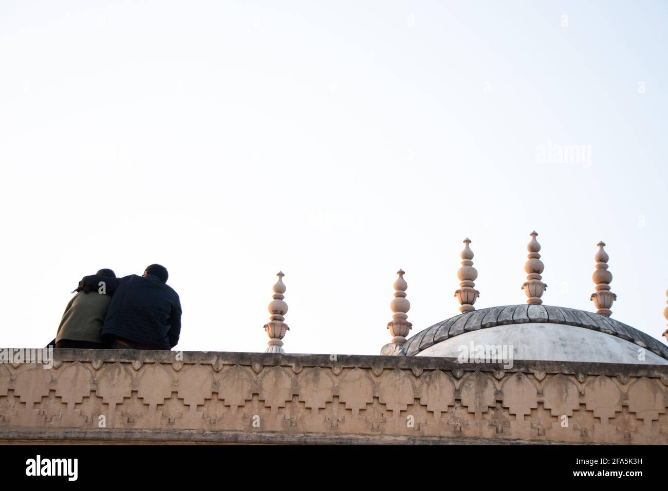 View at the backs of hugging couple sitting on top of a historical ...