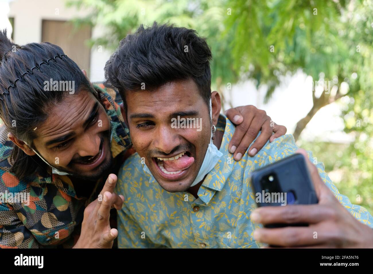 Funny Indian male friends with medical face masks under their chin taking a  selfie showing tongue Stock Photo - Alamy