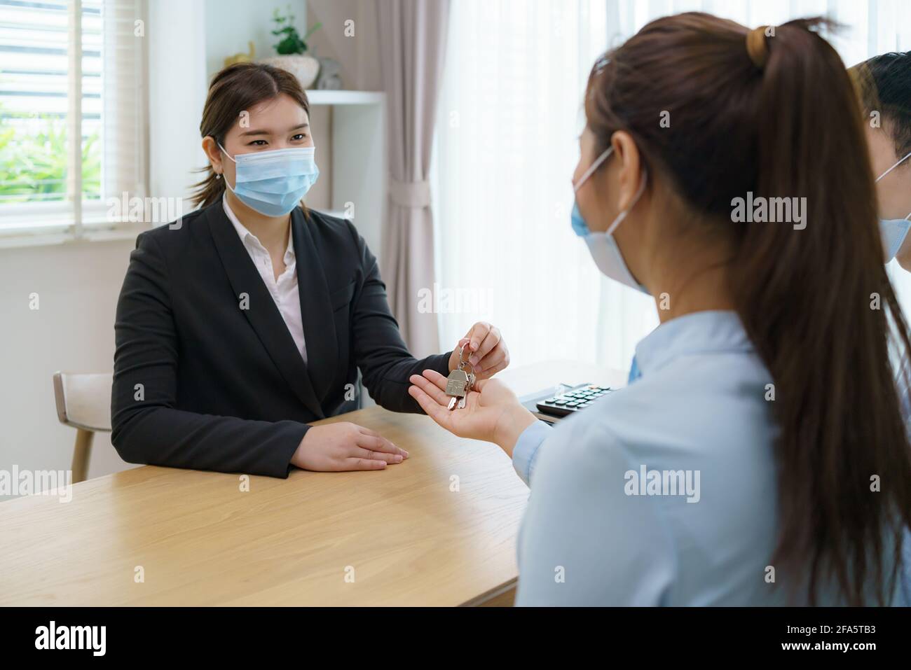 Asian Real estate agent woman give keys to customer after signing contract to buy house, insurance or loan real estate while wearing masks to prevent Stock Photo