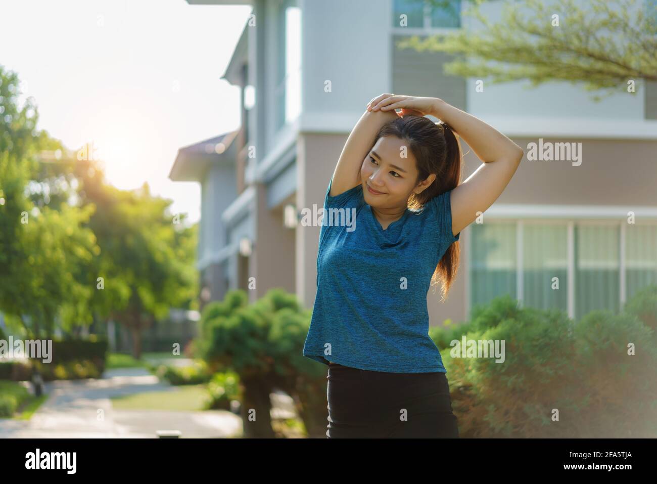 Asian woman stretching to warm up or cool down, before or after exercise, near the front door in the neighborhood for daily health and well being, bot Stock Photo