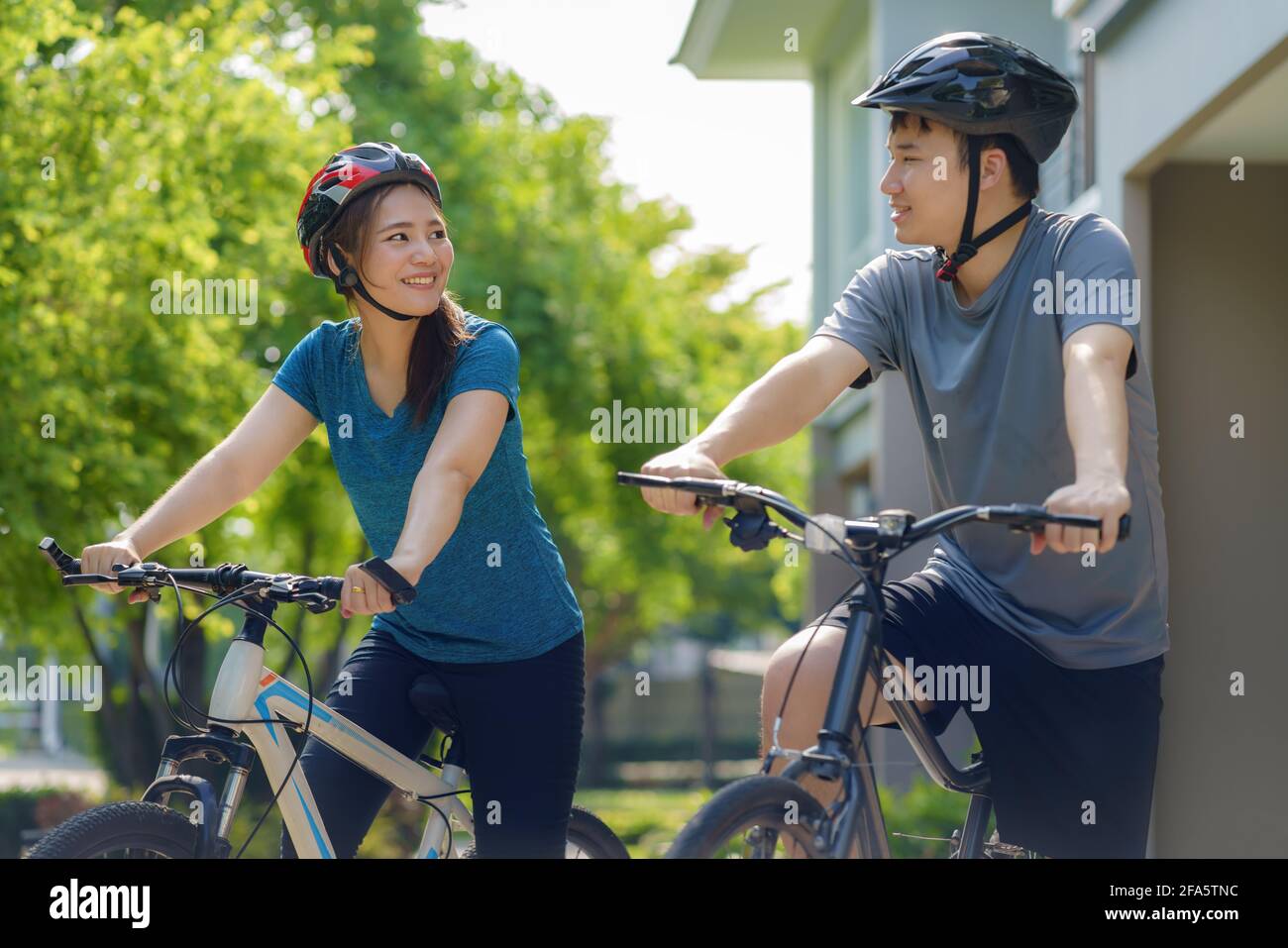 Asian couple wearing a helmet while preparing for a bike ride around her neighborhood for daily health and well being, both physical and mental. Stock Photo