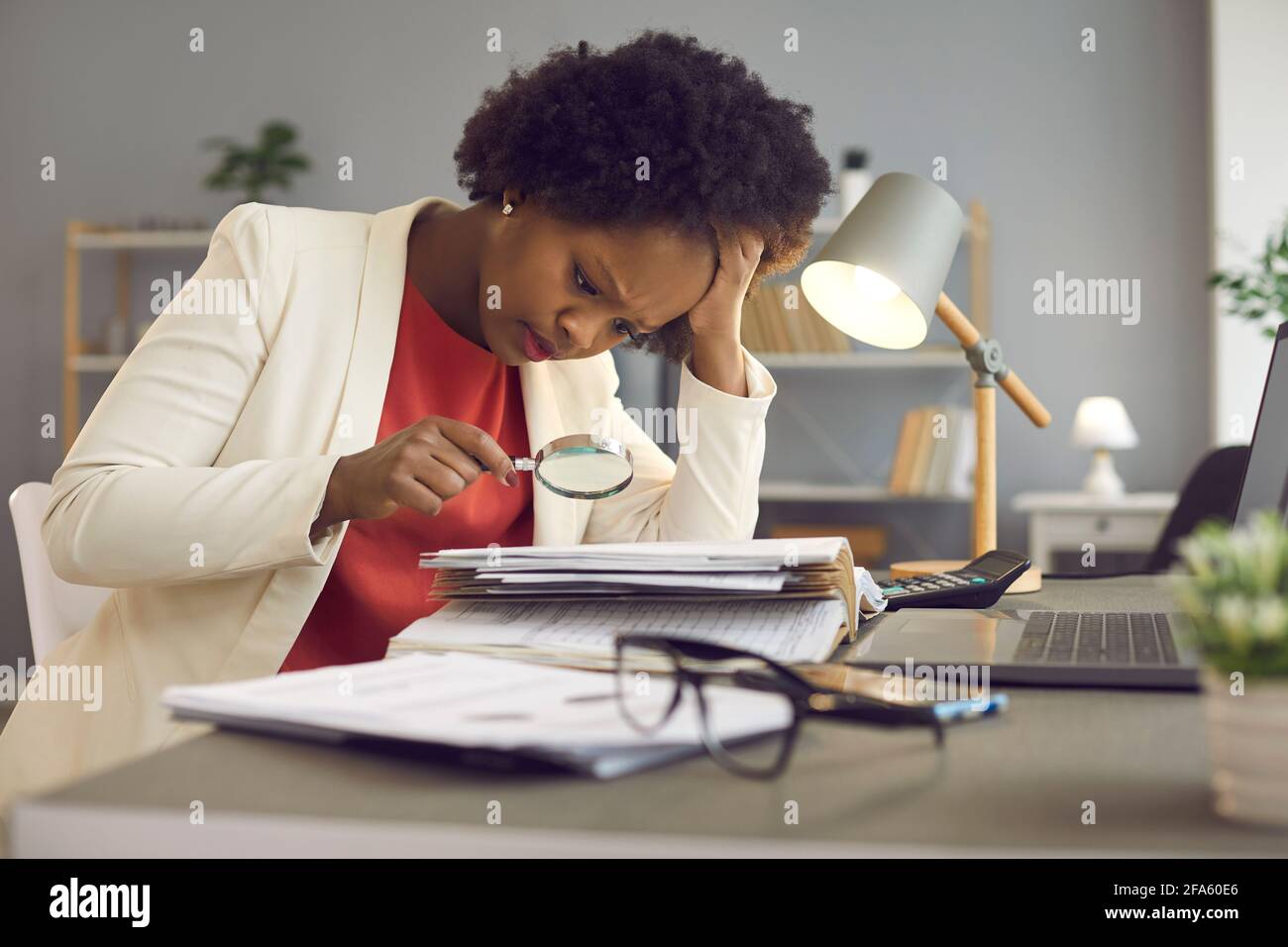 Focused woman uses a magnifying glass to check documents and look for an error in the accounts. Stock Photo
