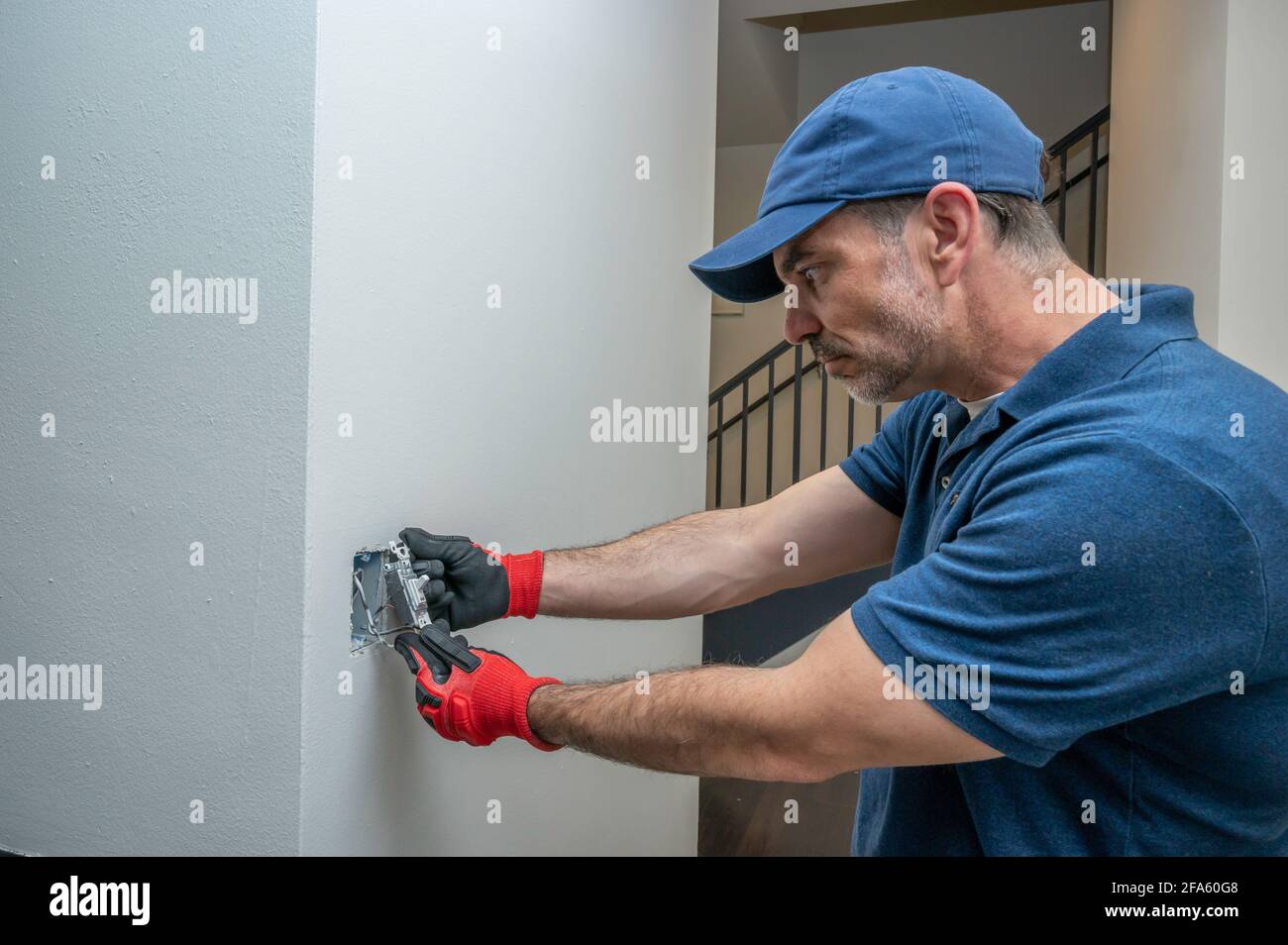 Electrician installing a low voltage toggle switch in a hallway Stock Photo