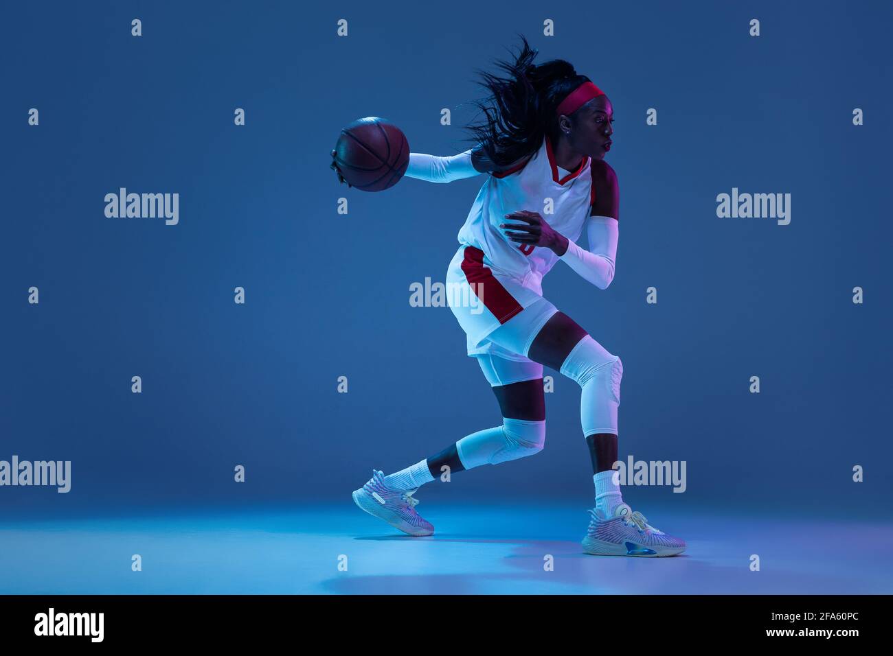 Beautiful africanamerican female basketball player in motion and action in neon light on blue