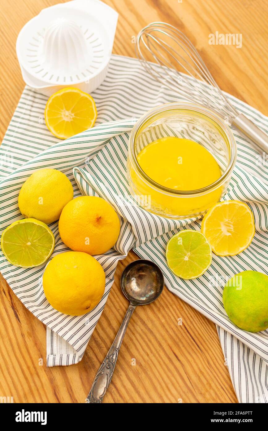 A lot of citrus fruits like lemons, oranges and limes on a wooden table ready to be squeezed for juice or for baking, a glass wtih lemon curd. Stock Photo