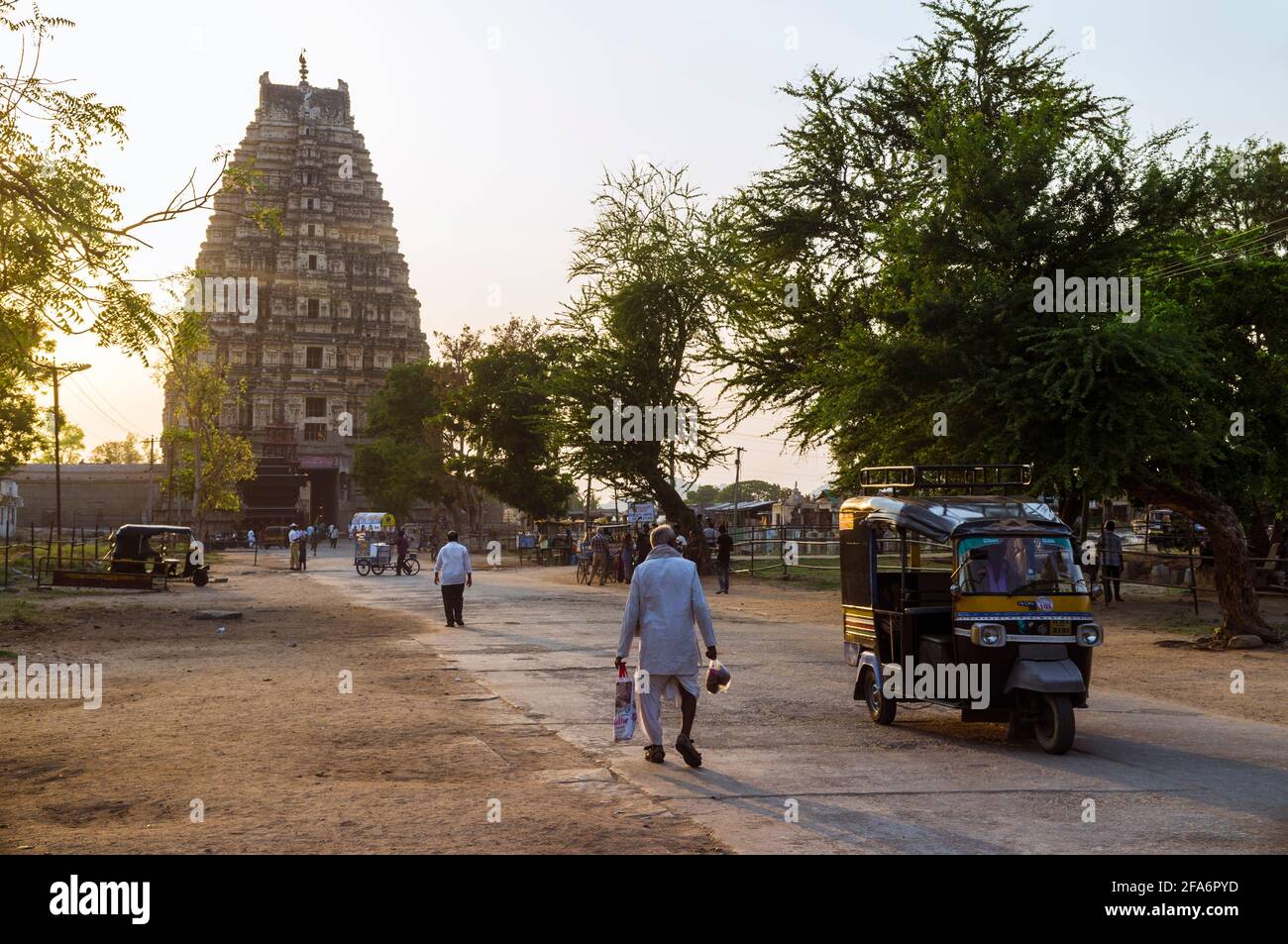 Hampi, Karnataka, India: An auto-rickshaw drives past a man walking at sunset towards the 7th century Sree Virupaksha Temple. Believed to be uninterru Stock Photo