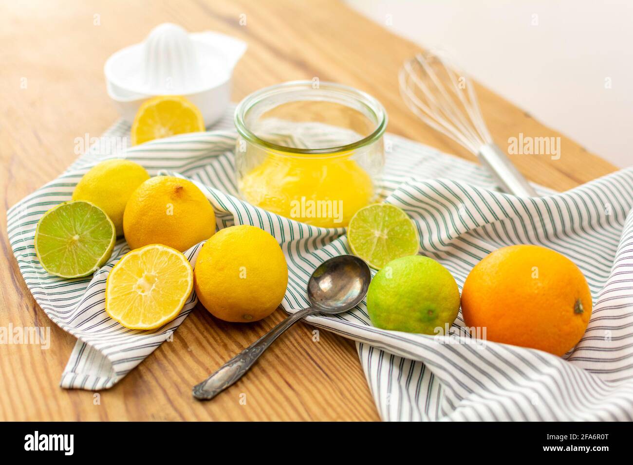 A lot of citrus fruits like lemons, oranges and limes on a wooden table ready to be squeezed for juice or for baking, a glass wtih lemon curd. Stock Photo