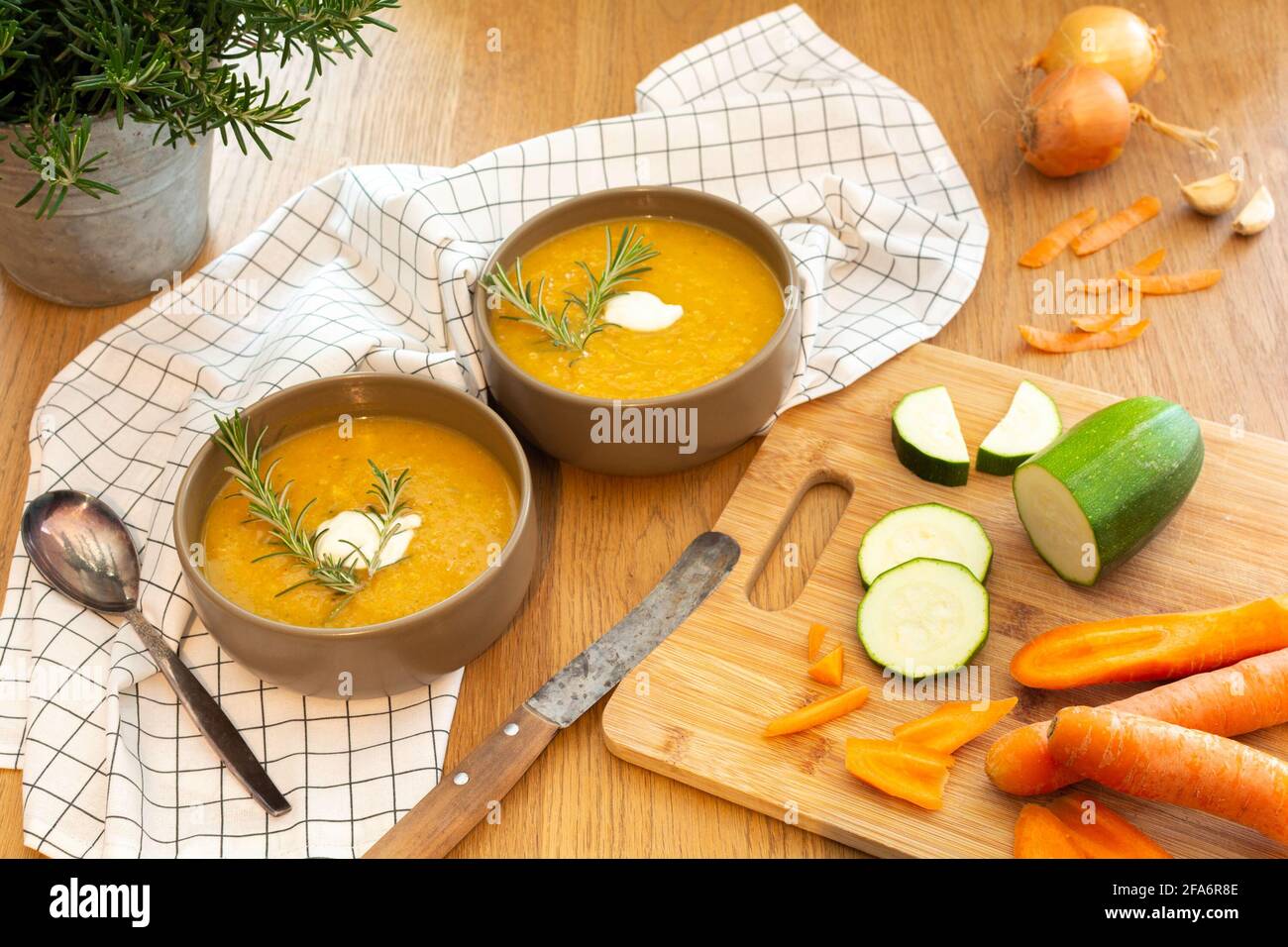 A nice homecooked meal containing a fresh vegetable soup with carrots and zucchini and onions served on an old wood table with a lot of garnish. Stock Photo