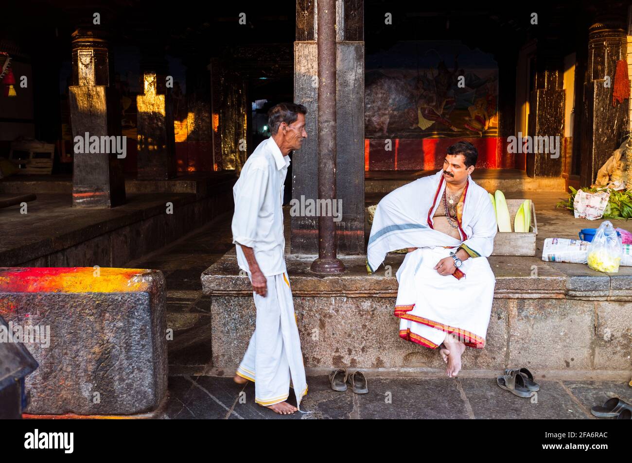 Udupi, Karnataka, India : A man walks past a brahmin priest sitting at the entrance of the 13th century Krishna temple. The temple was founded by the Stock Photo