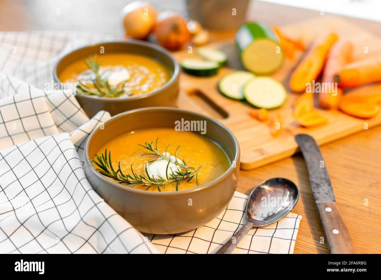 A nice homecooked meal containing a fresh vegetable soup with carrots and zucchini and onions served on an old wood table with a lot of garnish. Stock Photo