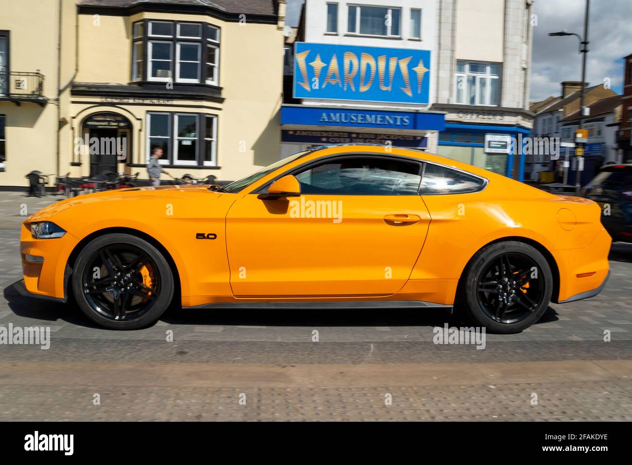 Bright yellow Ford Mustang 5L muscle car driving along Marine Parade in Southend on Sea, Essex, UK, passing Stardust amusement arcade Stock Photo