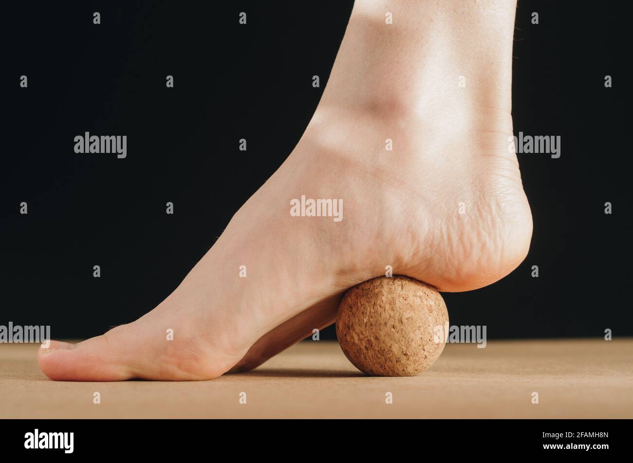 Artistic isolated close up video of foot on cork massage ball on cork yoga block for plantar fascia massage and hydration on black background Stock Photo