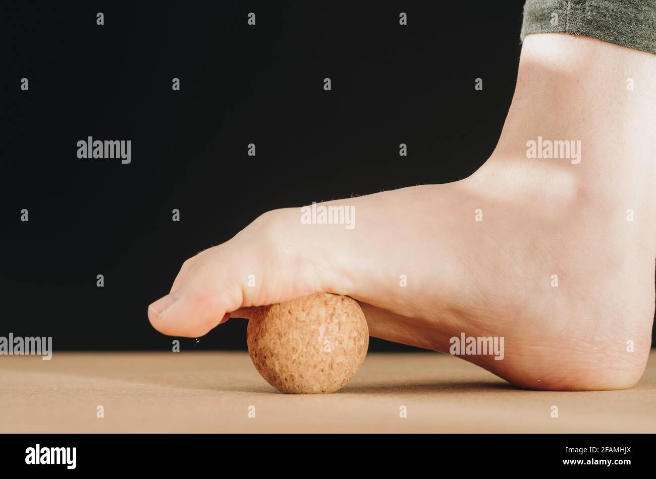 Artistic isolated close up foot on cork massage ball on cork yoga mat for plantar fascia massage and hydration on black background with copy space Stock Photo