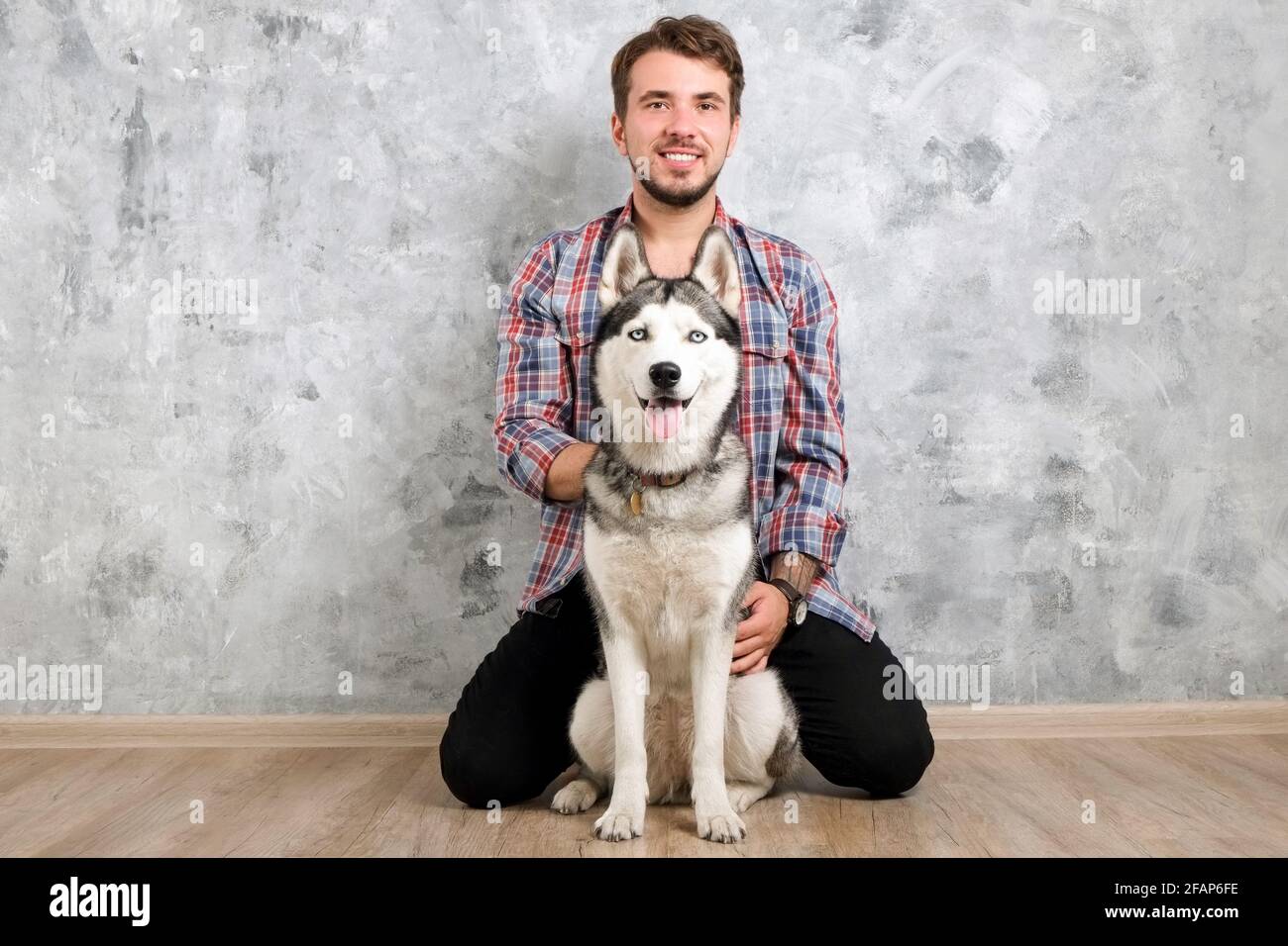 Young bearded man hanging out out with his husky dog. Hipster male wearing checkered flannel shirt and grey tank top spending quality time with four l Stock Photo