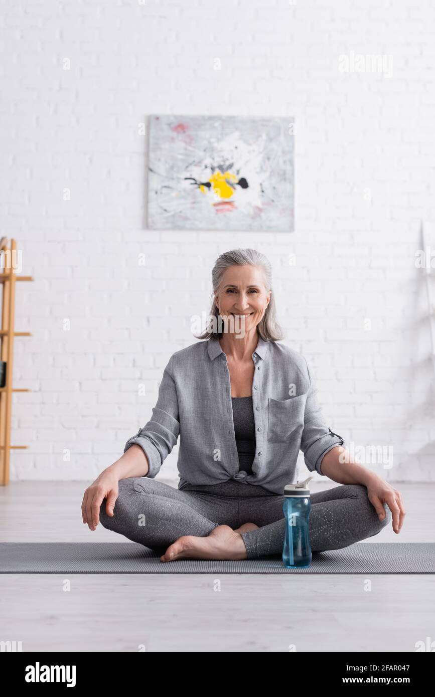 happy middle aged woman sitting in lotus pose on yoga mat Stock Photo ...