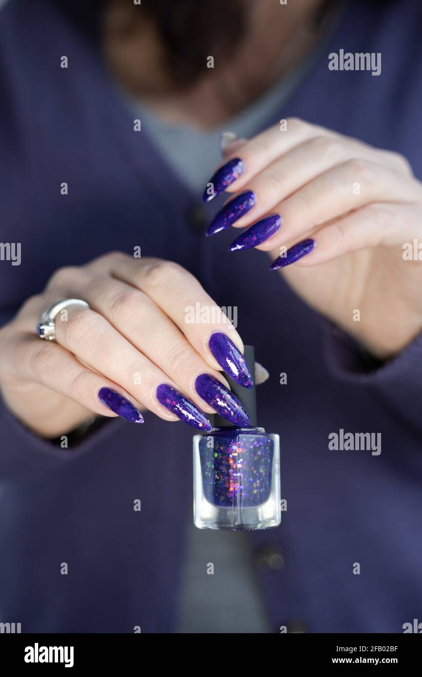 Female hand with long nails and purple lilac manicure holds a bottle of nail  polish Stock Photo - Alamy