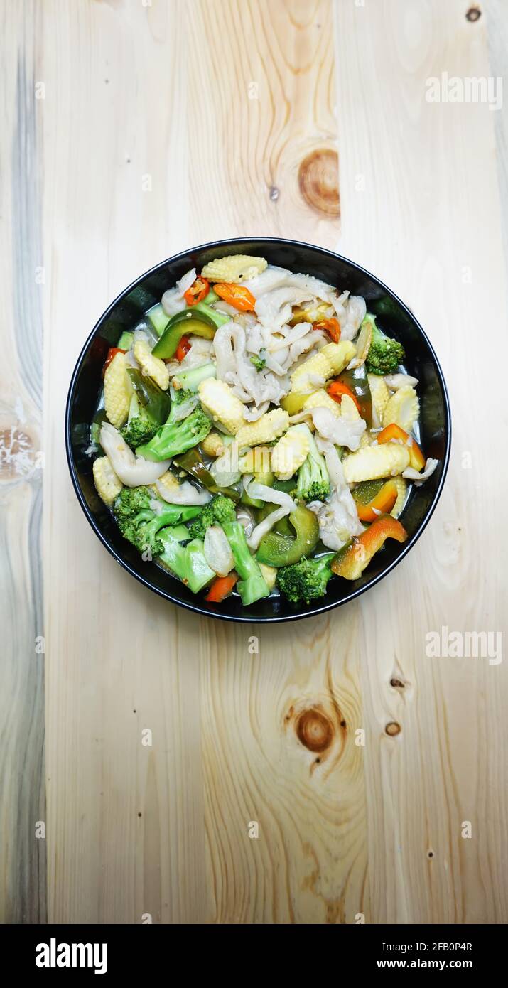 Vegetable capcay young corn with mushrooms and also peppers against a wooden background dyed black Stock Photo