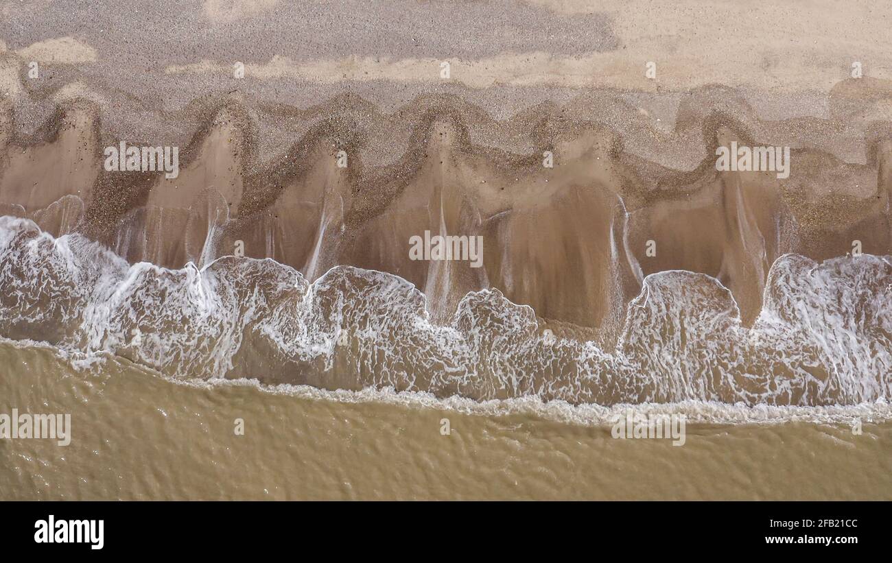 aerial view of waves breaking onto beach creating patterns in the sand Stock Photo