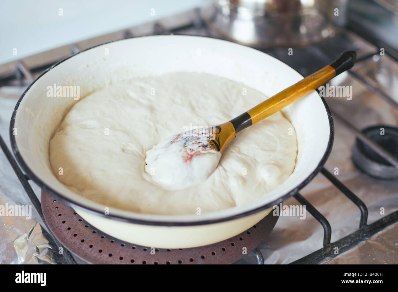 Yeast dough and wooden spoon in enameled bowl on stove Stock Photo