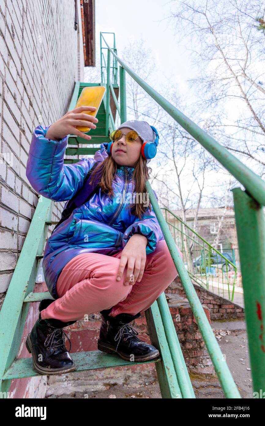 Girl in shiny jacket and sunglasses stay on the stairs. Wellness concept Stock Photo
