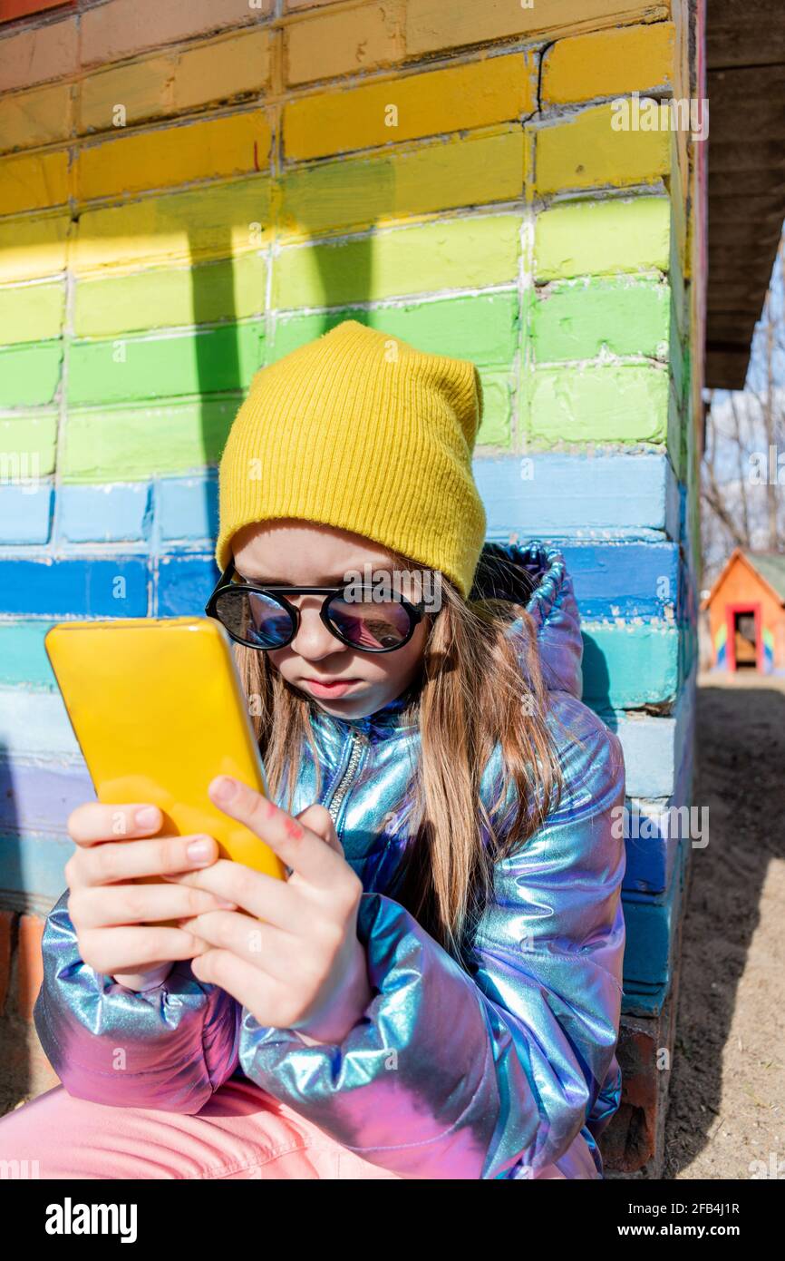 Teenage girl sits outdoors and looks into her smartphone. Concept wellness and technology use child Stock Photo