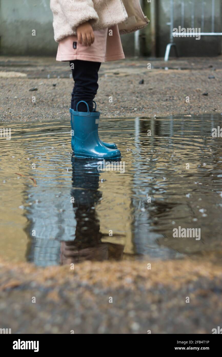 Low Section Reflection Of A Girl In Rubber Boots Standing In A Puddle 