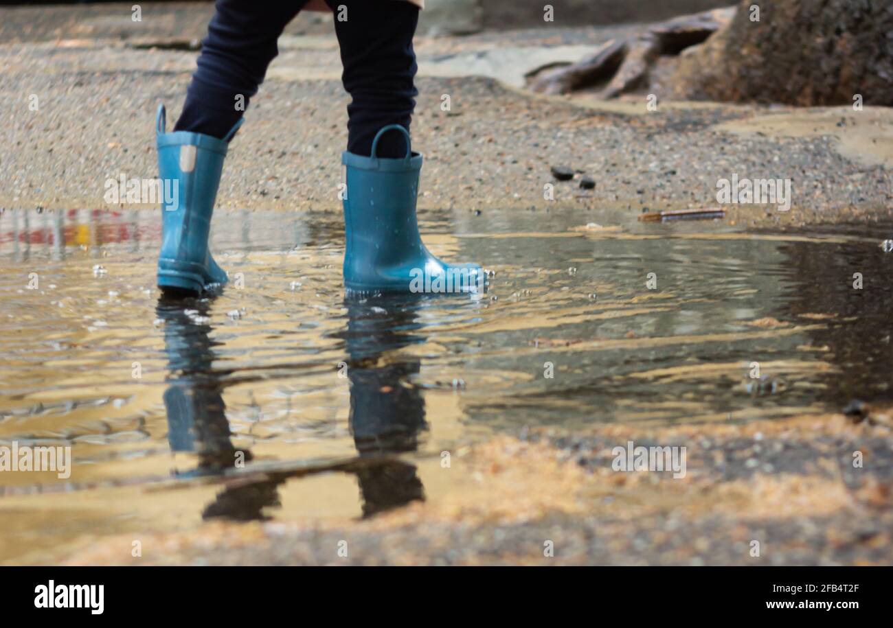 Low section reflection of a girl in rubber boots standing in a puddle ...