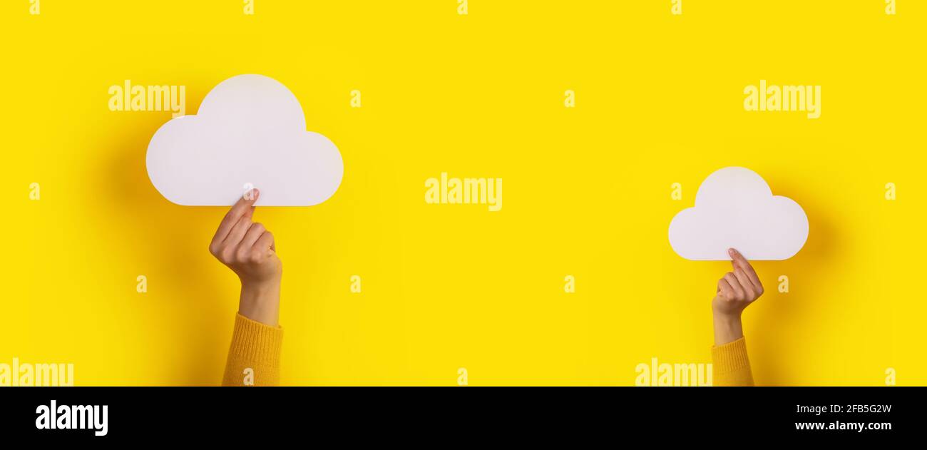 Two hands holding paper cloud over yellow background, panoramic image, cloud storage concept Stock Photo