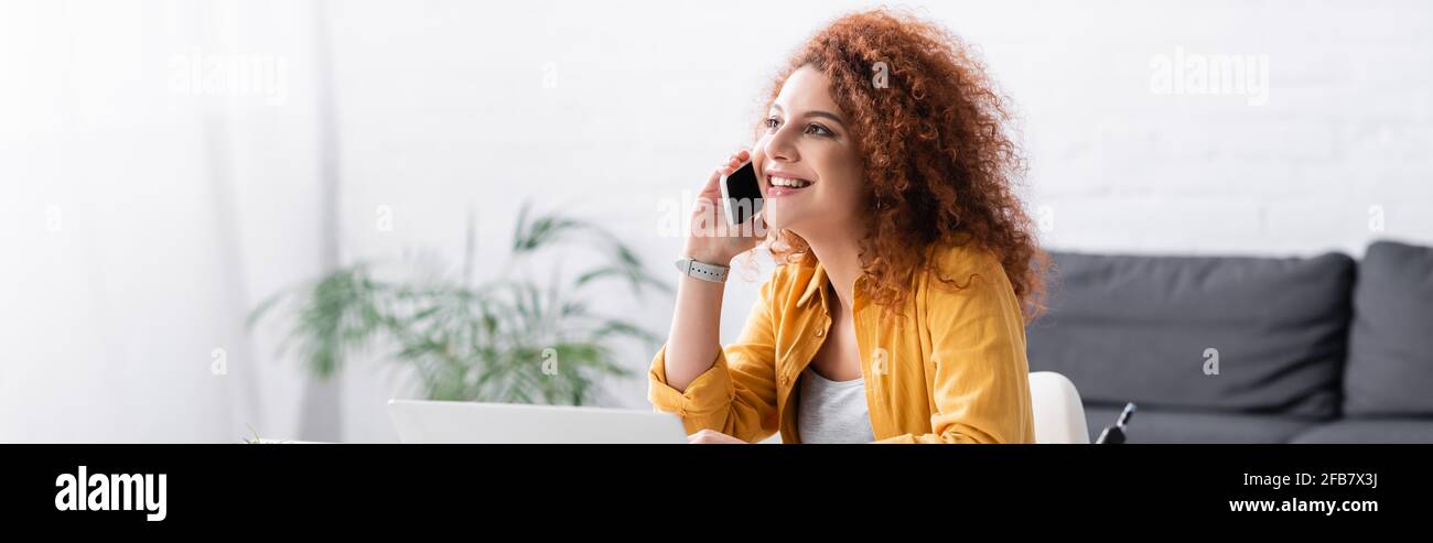 joyful freelancer with curly hair talking on cellphone at home, banner Stock Photo