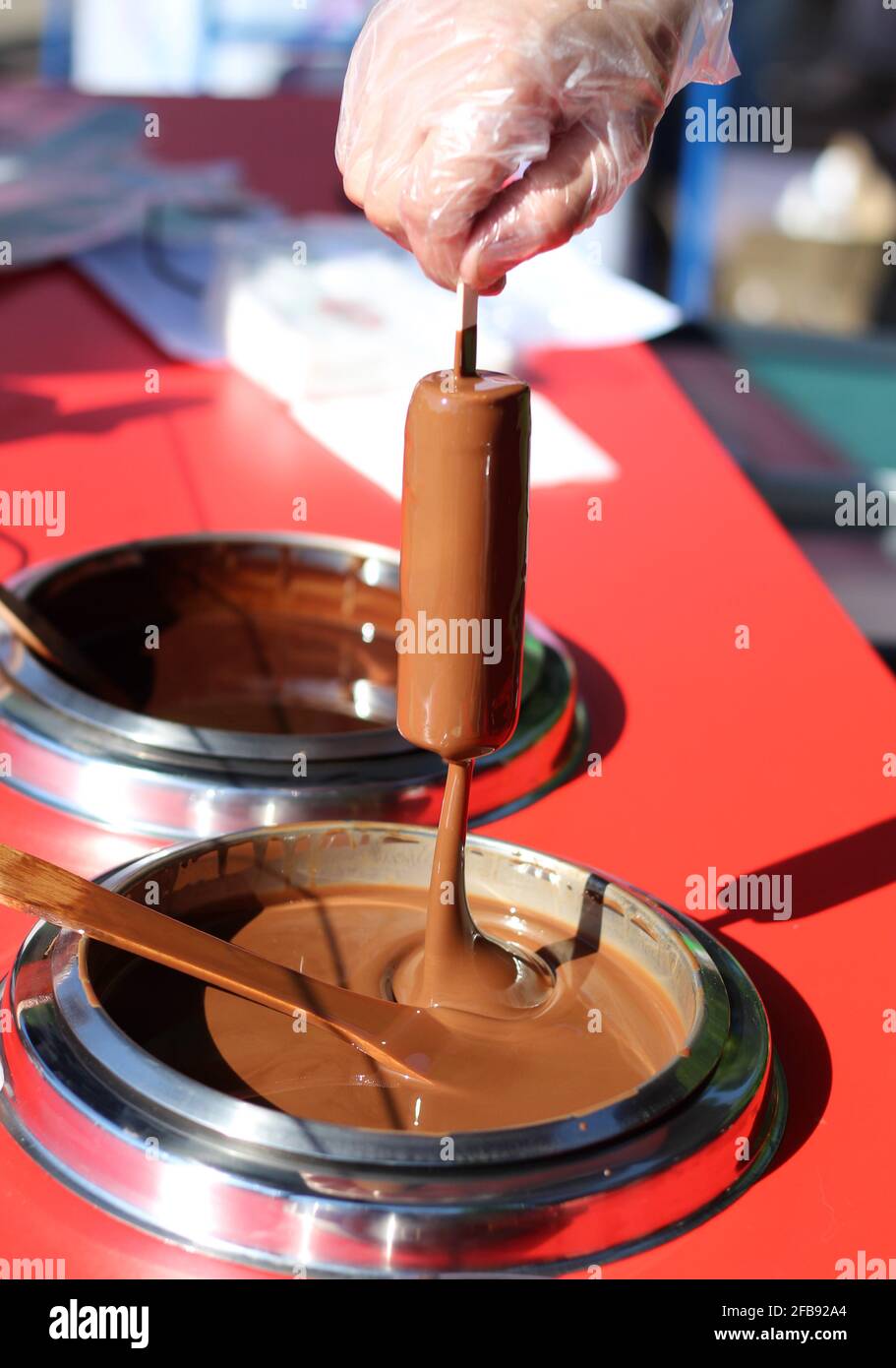 The men's hand in gloves putting icecream to the liquid chocolate