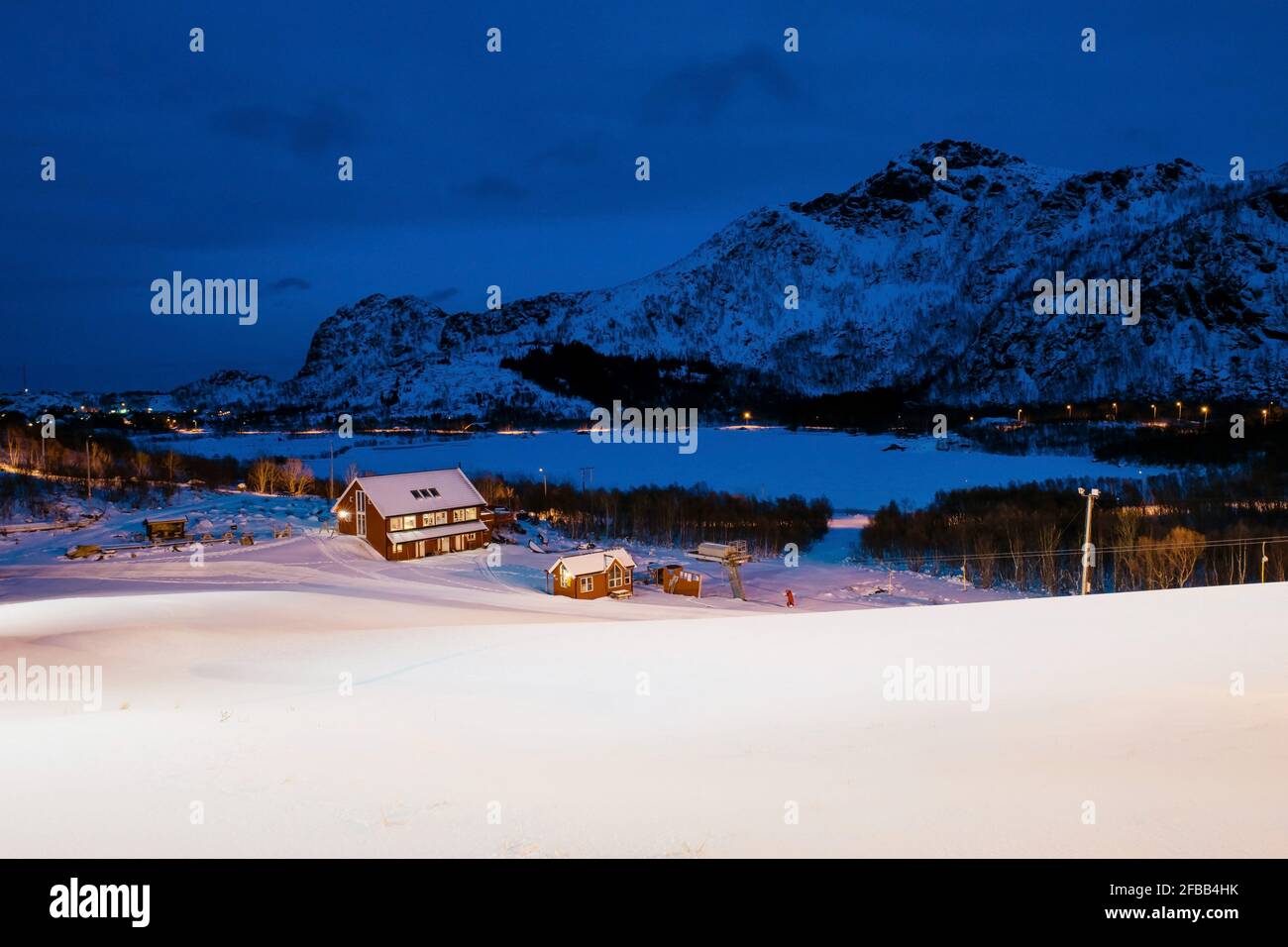 Beautiful view of norwegian village with small red houses covered with snow among rocky mountains. Winter twilights on Lofoten islands. Stock Photo