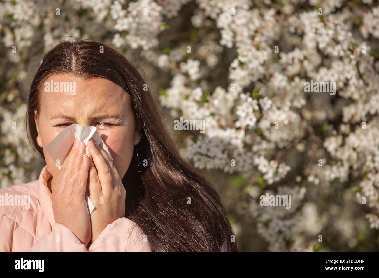 Spring allergy symptoms concept, young woman sneezing in front of