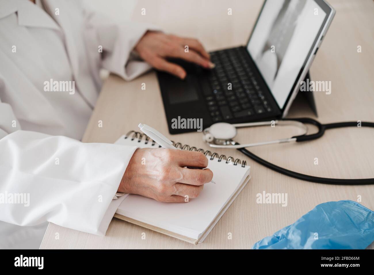 Female doctor using digital tablet while writing in diary at desk in medical clinic Stock Photo