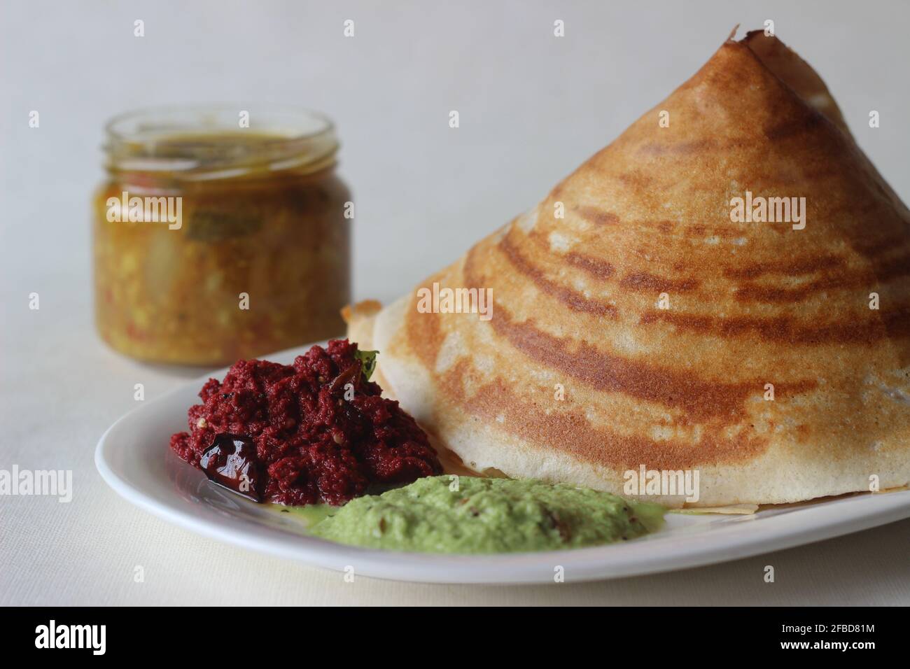 Crispy pancake made of rice and lentils folded in a cone shape. Served with spicy beetroot coconut condiments, coriander coconut condiments and sambar Stock Photo